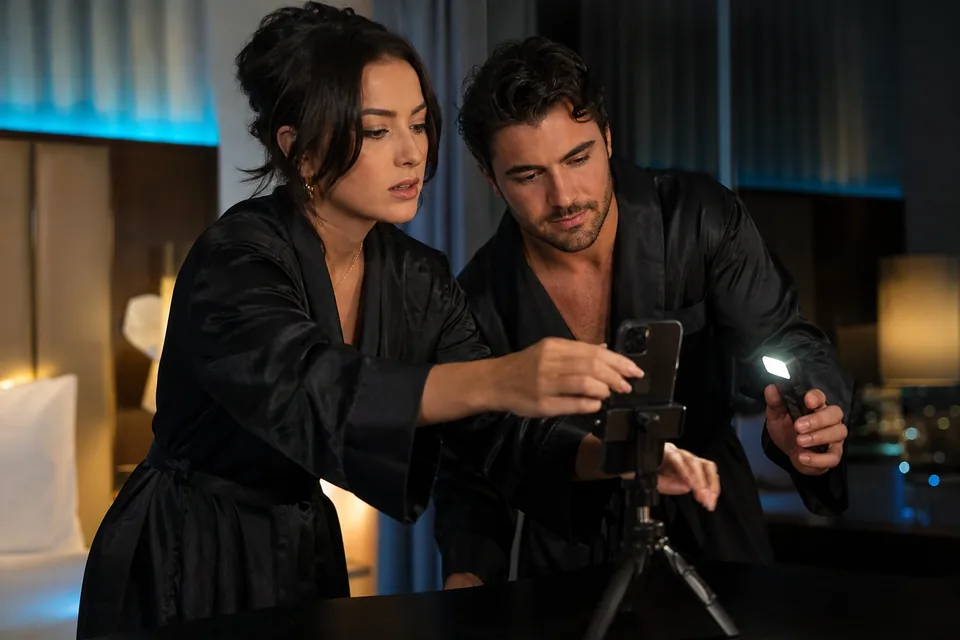 Couple in silk robes setting up a phone on a tripod in a hotel suite