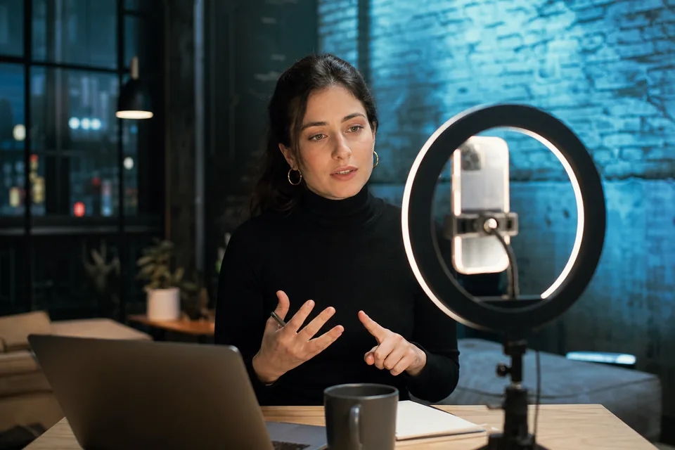 Creator recording a video on her phone under a ring light in a loft studio